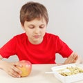 Young boy at the table chooses between instant noodles and apple on white background