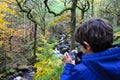 Young boy taking photograph of forest and stream