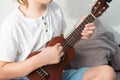 Young boy tuning ukulele at home. Blond haired boy sitting on couch playing acoustic guitar Royalty Free Stock Photo