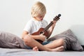 Young boy tuning ukulele at home. Blond haired boy sitting on couch playing acoustic guitar Royalty Free Stock Photo