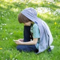 Young boy using smart phone at spring glade. Cute 11 years old boy sitting on green grass at spring park. Kid`s outdoor portrait