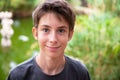 Young boy walking in summer park with trees near the pound. Cute happy smiling teen boy 13 years old looking at camera outdoor. Royalty Free Stock Photo