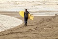 Young boy walking toward ocean with wetsuit and yellow surfboard - almost monochromatic in browns and ochers