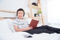 Young boy wearing headset listening music and reading book on bed