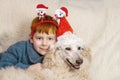 A young boy wearing a santa hat smiles and hugs a large white royal poodle dog. The relationship between a dog and a child Royalty Free Stock Photo