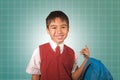 Young boy 7 or 8 years old in vest and necktie uniform holding bag smiling cheerful in front of green chalkboard excited about Royalty Free Stock Photo