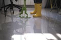 young boy in yellow rubber boots diligently cleaning up the aftermath of a flood in his apartment. With a mop in hand he