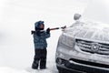 A little boy brushing snow from a car