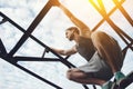 Young brave man climbing and sitting on high metal construction