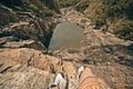 Young brave man sitting on a high stone cliff above little lake. Top view. Royalty Free Stock Photo