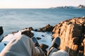 Young brave traveler resting on rock in front of snowy cliff and blue ocean and look on feet. POV view on legs and shoes on backgr