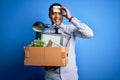 Young brazilian businessman holding box wearing reminder paper with fired message stressed with hand on head, shocked with shame