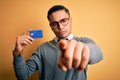 Young brazilian businessman holding credit card money over isolated yellow background pointing with finger to the camera and to Royalty Free Stock Photo