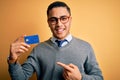 Young brazilian businessman holding credit card money over isolated yellow background very happy pointing with hand and finger Royalty Free Stock Photo