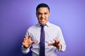 Young brazilian businessman wearing elegant tie standing over isolated purple background smiling funny doing claw gesture as cat,