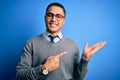 Young brazilian businessman wearing tie standing over isolated blue background amazed and smiling to the camera while presenting