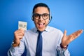 Young brazilian call center agent man overworked holding reminder paper with help message very happy and excited, winner