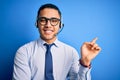 Young brazilian call center agent man wearing glasses and tie working using headset with a big smile on face, pointing with hand Royalty Free Stock Photo