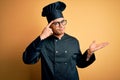 Young brazilian chef man wearing cooker uniform and hat over isolated yellow background confused and annoyed with open palm