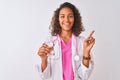 Young brazilian doctor woman holding glass of water standing over isolated white background very happy pointing with hand and Royalty Free Stock Photo