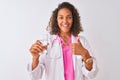 Young brazilian doctor woman holding glass of water standing over isolated white background very happy pointing with hand and Royalty Free Stock Photo