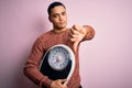 Young brazilian man doing diet to lose weigth holding scale over isolated pink background with angry face, negative sign showing