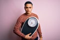 Young brazilian man doing diet to lose weigth holding scale over isolated pink background with a confident expression on smart