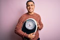 Young brazilian man doing diet to lose weigth holding scale over isolated pink background with a happy face standing and smiling