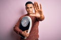 Young brazilian man doing diet to lose weigth holding scale over isolated pink background with open hand doing stop sign with