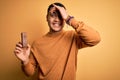 Young brazilian man eating healthy energy bar with protein over isolated yellow background stressed with hand on head, shocked Royalty Free Stock Photo