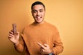 Young brazilian man eating healthy energy bar with protein over isolated yellow background very happy pointing with hand and Royalty Free Stock Photo