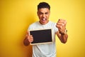 Young brazilian man holding blackboard standing over isolated yellow background annoyed and frustrated shouting with anger, crazy Royalty Free Stock Photo