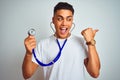 Young brazilian man holding stethoscope standing over isolated white background pointing and showing with thumb up to the side Royalty Free Stock Photo