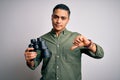 Young brazilian man looking through binoculars over isolated white background with angry face, negative sign showing dislike with Royalty Free Stock Photo