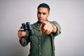 Young brazilian man looking through binoculars over isolated white background pointing with finger to the camera and to you, hand Royalty Free Stock Photo