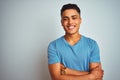 Young brazilian man wearing blue t-shirt standing over isolated white background happy face smiling with crossed arms looking at Royalty Free Stock Photo