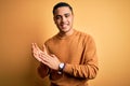 Young brazilian man wearing casual sweater standing over isolated yellow background clapping and applauding happy and joyful, Royalty Free Stock Photo