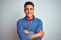 Young brazilian man wearing denim shirt standing over isolated white background happy face smiling with crossed arms looking at Royalty Free Stock Photo