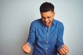 Young brazilian man wearing denim shirt standing over isolated white background very happy and excited doing winner gesture with Royalty Free Stock Photo