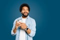 A young Brazilian man wearing a light blue denim shirt holds a smartphone and looks pensively to the side Royalty Free Stock Photo