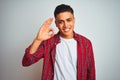 Young brazilian man wearing red shirt standing over isolated white background smiling positive doing ok sign with hand and fingers Royalty Free Stock Photo