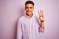 Young brazilian man wearing shirt standing over isolated pink background showing and pointing up with fingers number three while