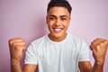 Young brazilian man wearing t-shirt standing over isolated pink background screaming proud and celebrating victory and success Royalty Free Stock Photo