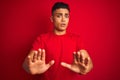 Young brazilian man wearing t-shirt standing over isolated red background Moving away hands palms showing refusal and denial with Royalty Free Stock Photo