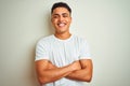 Young brazilian man wearing t-shirt standing over isolated white background happy face smiling with crossed arms looking at the Royalty Free Stock Photo