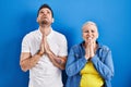 Young brazilian mother and son standing over blue background begging and praying with hands together with hope expression on face Royalty Free Stock Photo