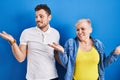 Young brazilian mother and son standing over blue background smiling showing both hands open palms, presenting and advertising