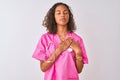 Young brazilian nurse woman wearing stethoscope standing over isolated white background smiling with hands on chest with closed