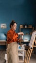 young brazilian woman artist in home studio stands near canvas mixes paints with brush on palette. Black hair, dressed