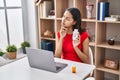 Young brazilian woman doing video call showing pills to the doctor serious face thinking about question with hand on chin, Royalty Free Stock Photo